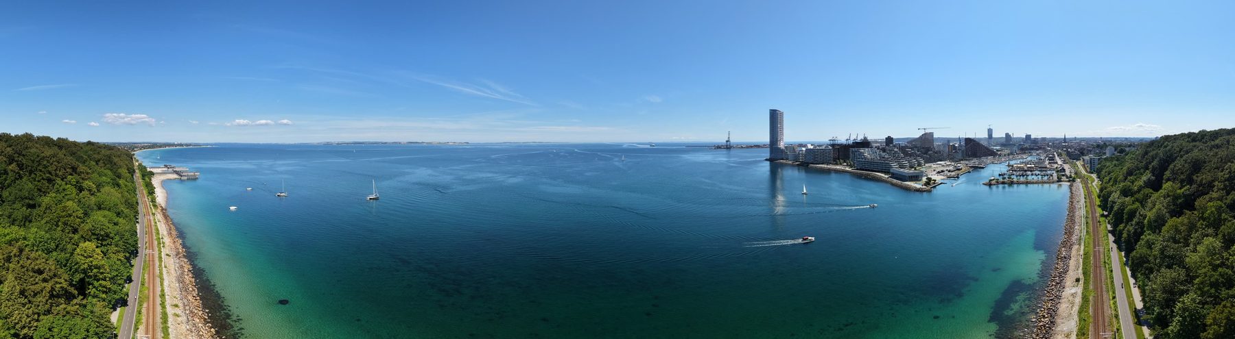 Wide aerial panorama of Aarhus Bay, from the wooded coast across the water to the harbour and city