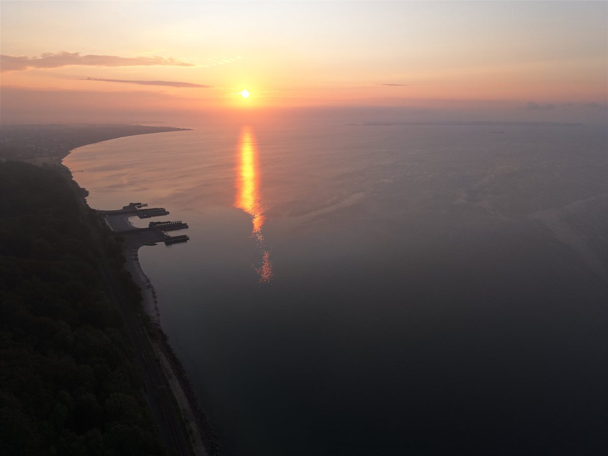 Sunrise over Aarhus Bay from the air, the sun's reflection running across calm water toward the coast